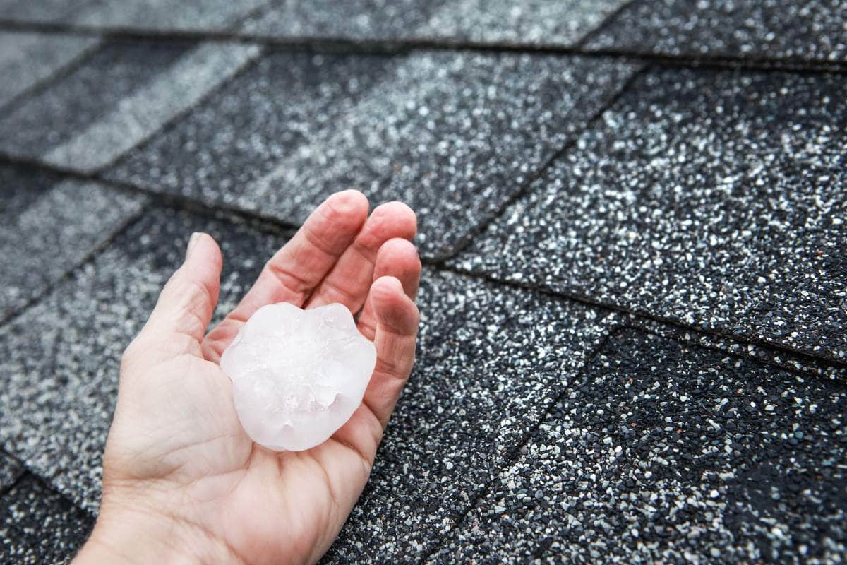 Large Hailstone Held In Hand Over Asphalt Shingle Roof, Showing Potential Storm Damage Risk – AllDone Construction